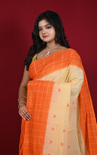 A woman wearing a bright orange and cream checkered saree with a checkered border, standing against a solid dark red background.