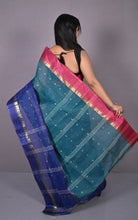 Woman wearing a blue and pink saree against a gray background