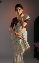 Model holding the pallu of an off-white Jamdani saree showing soft fabric pleats and contrast embroidery.